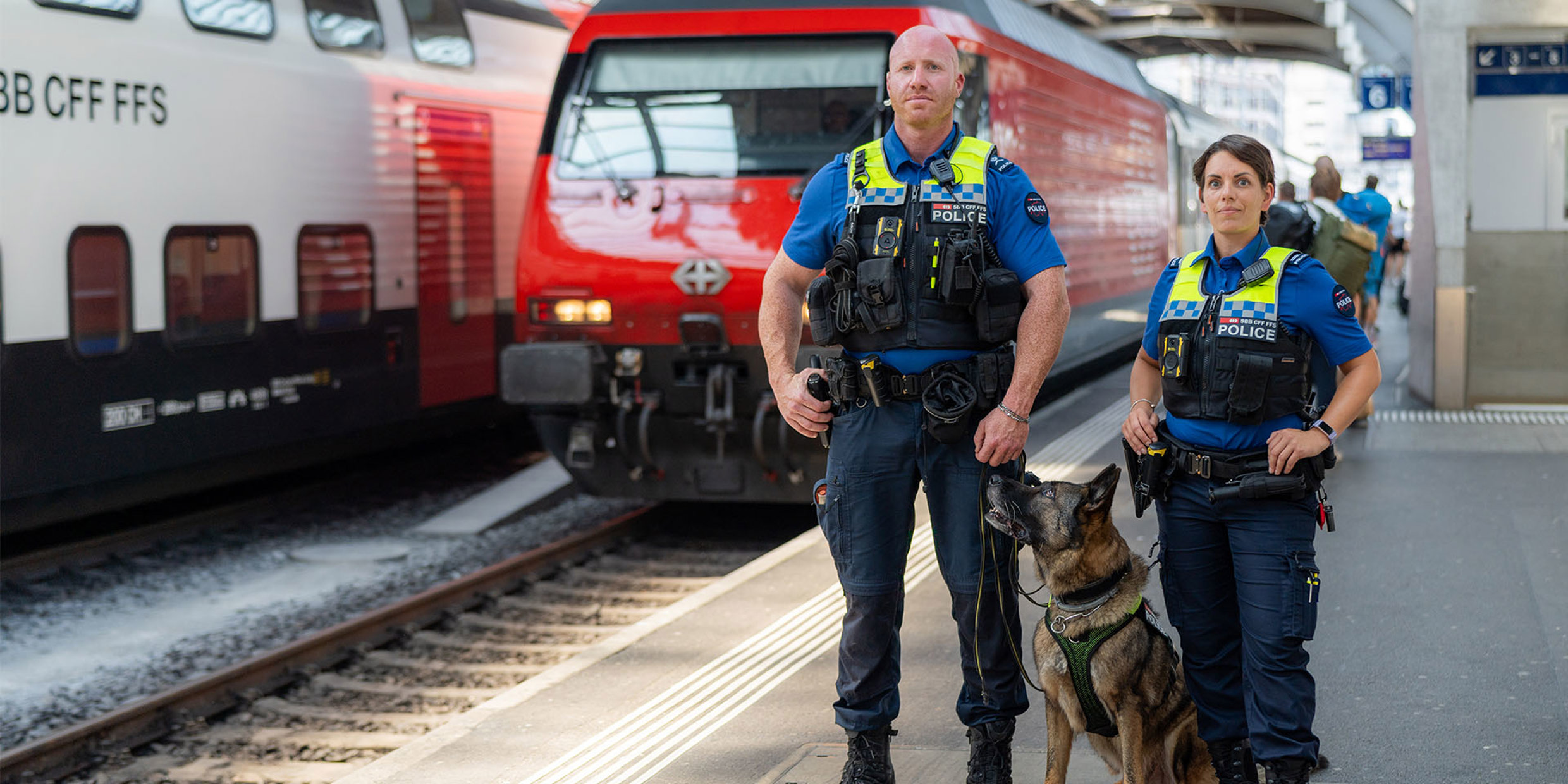 Zwei Sicherheitsbeamte der SBB auf dem perron und ein Zug fährt im Hintergrund ein.